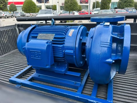 Blue industrial electric motor and pump assembly mounted on a trailer bed in a parking lot
