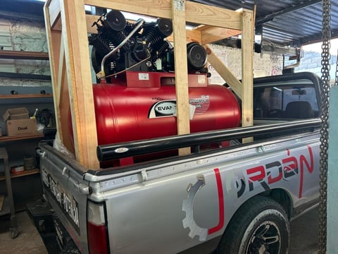 Air compressor with red tanks mounted on wooden frame in pickup truck bed