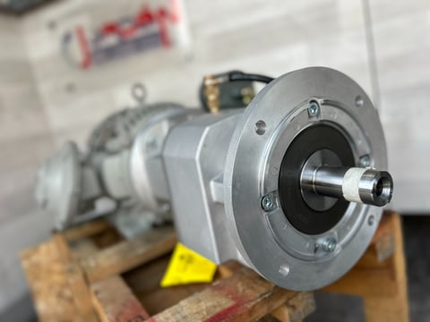 Close-up of a silver industrial gear pump with flanged mounting on a wooden base in a workshop setting