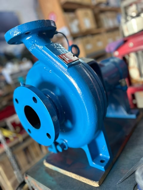 Close-up of a bright blue industrial pump with flanged ports, mounted on a base in a workshop setting