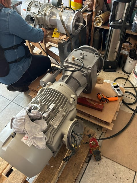 Technician working on industrial electric motors and pump equipment in a workshop setting