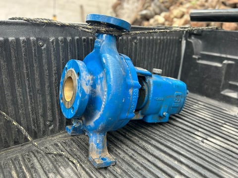 Blue industrial centrifugal pump mounted on a dark metal surface in an outdoor setting